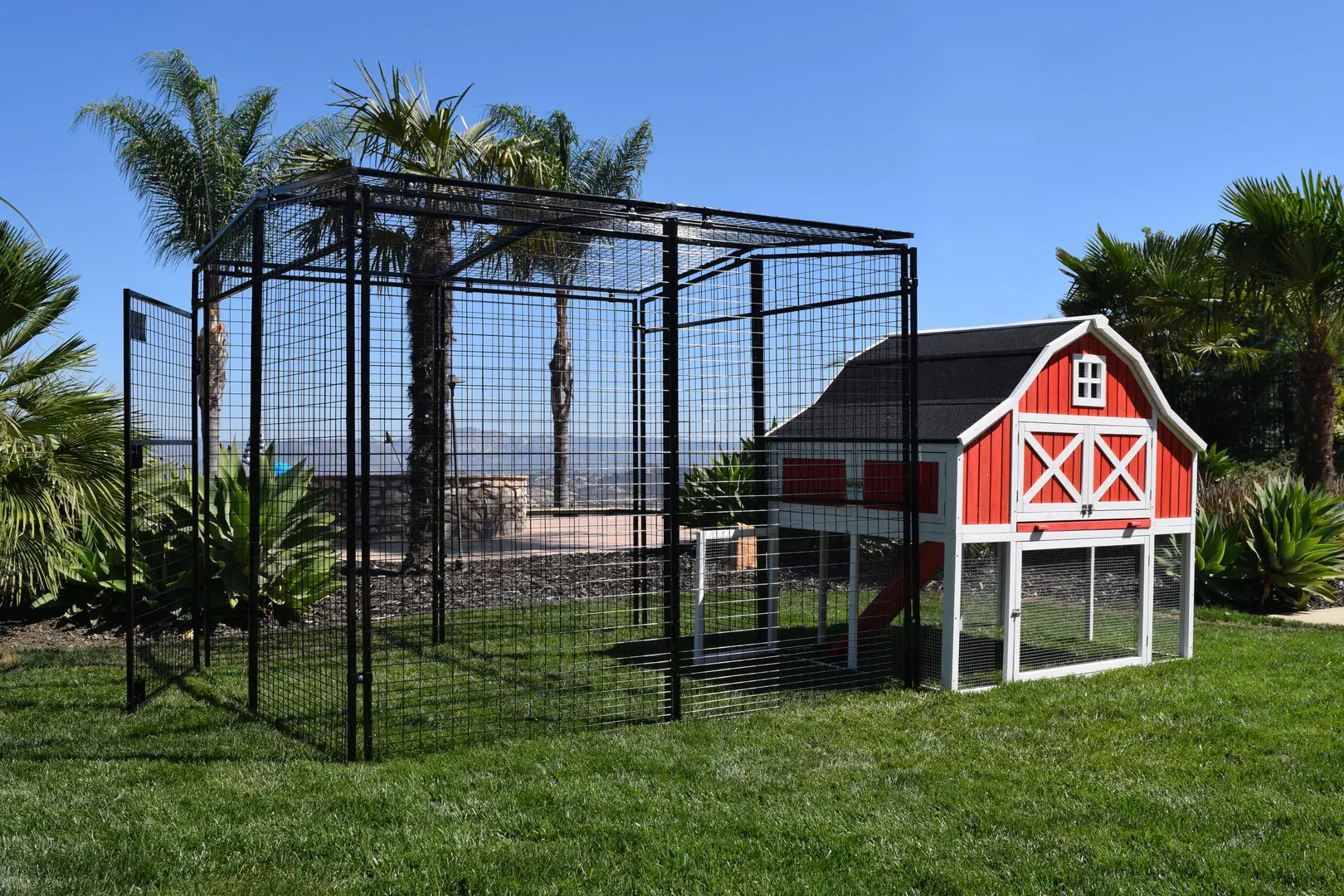 A red barn and chicken coop in the grass.